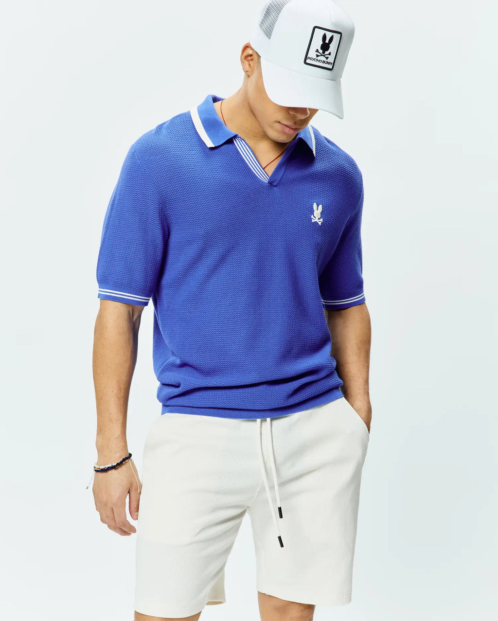 Mens Innis Polo, a royal blue classic fit pique knit polo with a V-neck, white striped collar, white striped sleeve cuffs, and a small embroidered white Psycho Bunny skull logo on the left chest.