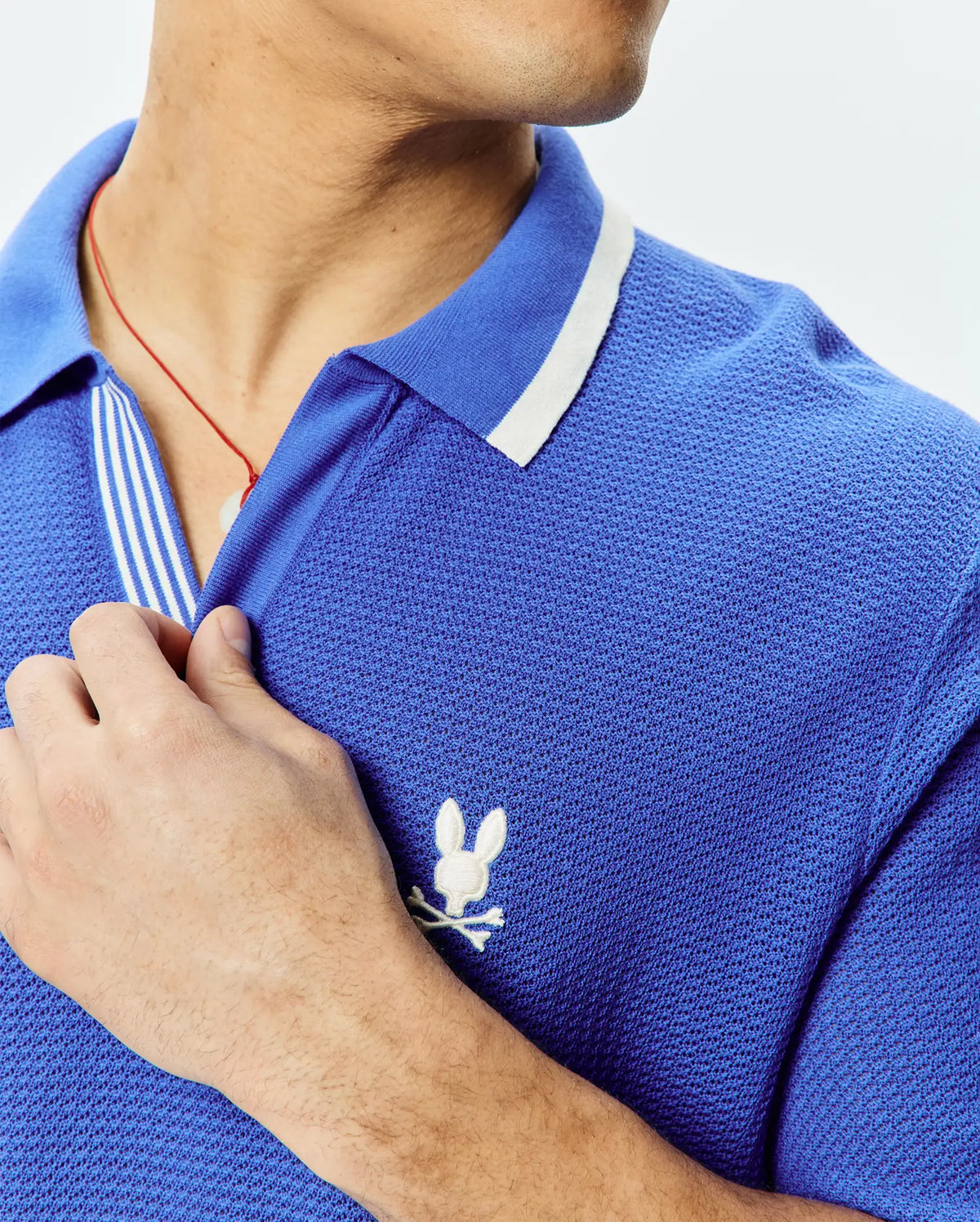 Mens Innis Polo, vibrant blue pique knit polo shirt with a classic fit, featuring a white striped collar, striped placket, and a small white embroidered Psycho Bunny skull logo on the left chest.