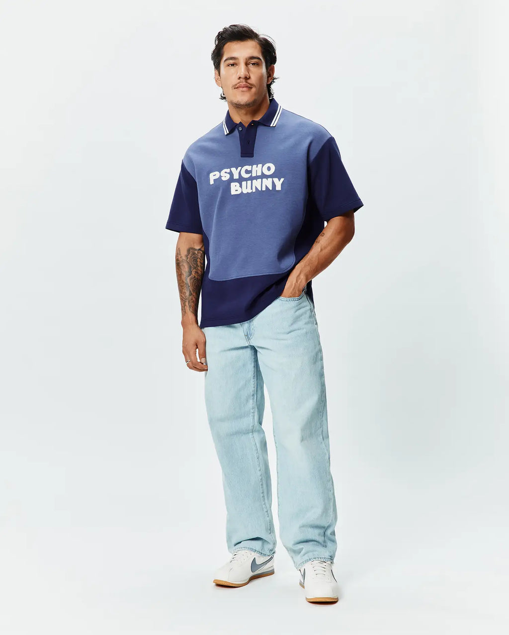 Mens Kelly Oversized Polo, a two-tone blue color block jersey polo with an oversized fit, featuring white collar stripes and a large white PSYCHO BUNNY text logo across the chest.