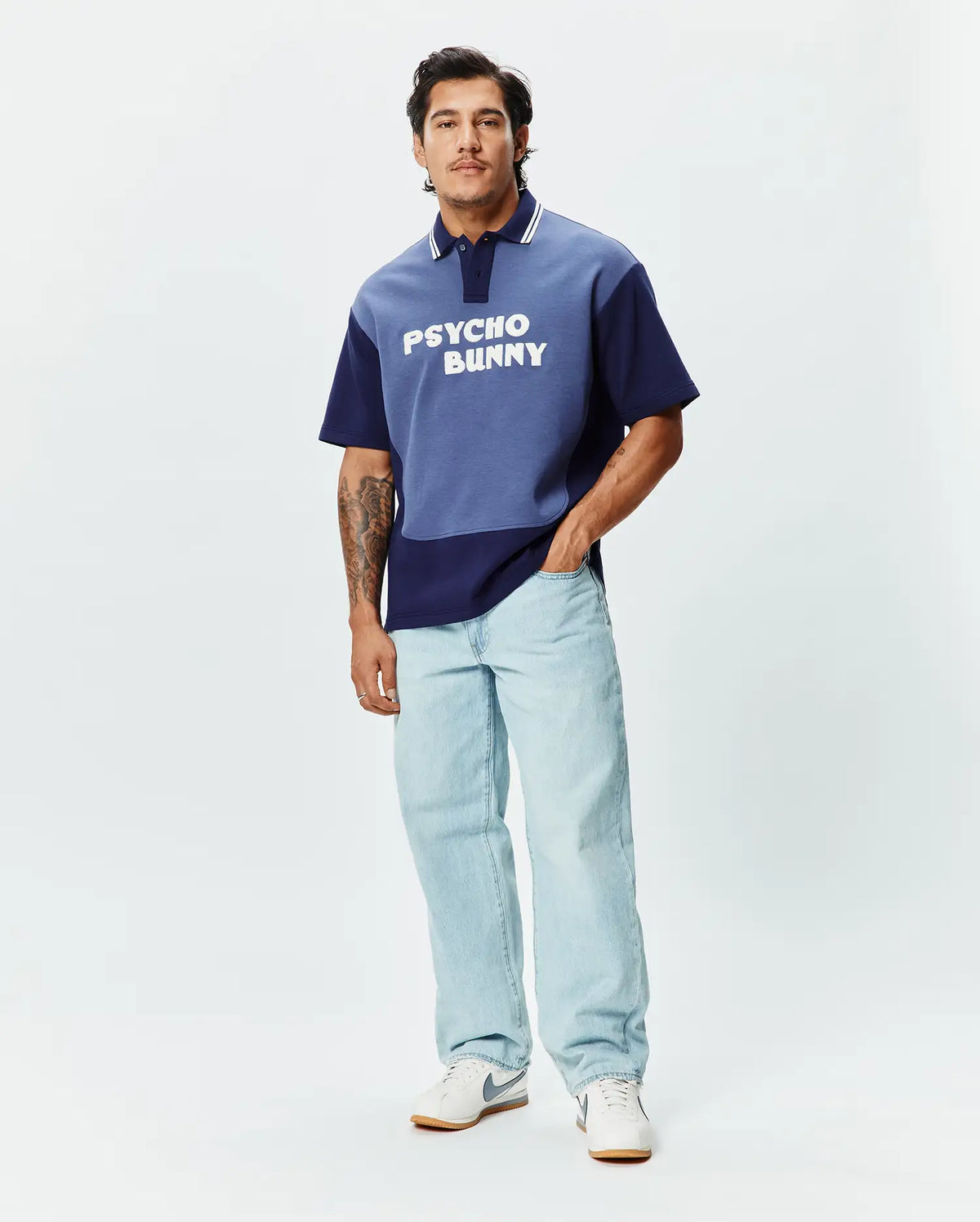 Mens Kelly Oversized Polo, a two-tone blue color block jersey polo with an oversized fit, featuring white collar stripes and a large white PSYCHO BUNNY text logo across the chest.
