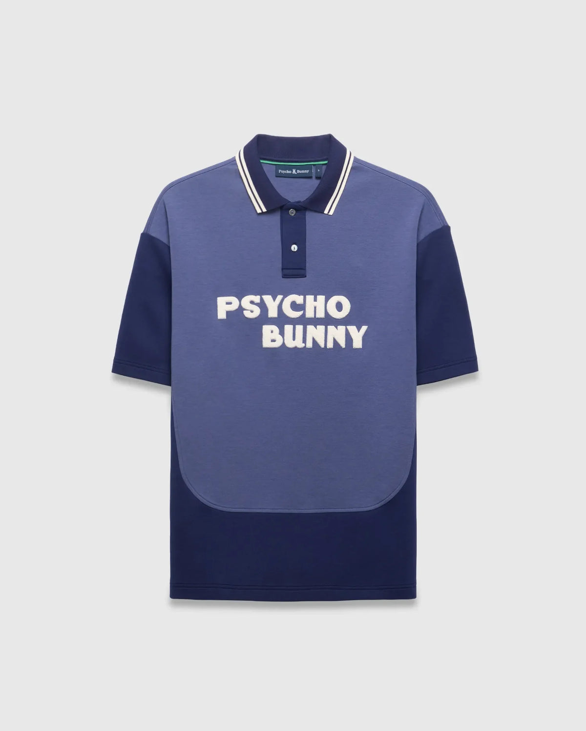 Mens Kelly Oversized Polo, an oversized two-tone blue jersey polo with medium blue and navy color-block, white-striped navy collar, large white embroidered PSYCHO BUNNY chest text, and small back neck bunny skull logo.